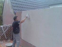 Ein Mann verputzt die Wand eines Hauses mit einer Kelle.