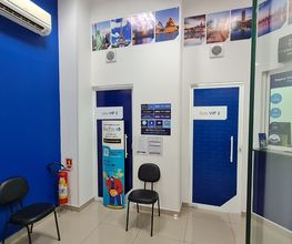Sala de espera com paredes e portas azuis, cadeiras pretas e fotos de paisagens na parede superior.