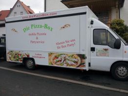 Pizza-Foodtruck mit Aufschrift "Die Pizza-Box" und Werbetext für Partyservice auf der Straße.