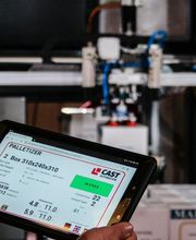 Persona controla máquina industrial con tablet; pantalla muestra datos de paletización.