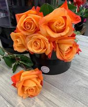 Ramo de rosas naranjas en un jarrón negro sobre una mesa de madera.