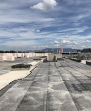 Betondach mit Baumaterialien, blauer Himmel und Wolken im Hintergrund.