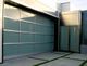 Modern glass garage door next to a metal entrance door in a contemporary building.