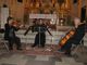 Trío de cuerdas tocando en una iglesia, con violín, viola y violonchelo frente a un altar.