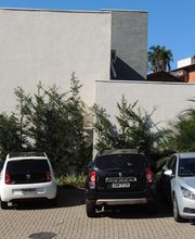 Três carros estacionados em frente a um prédio branco com árvores e arbustos ao redor.