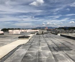 Betondach mit Baumaterialien, blauer Himmel und Wolken im Hintergrund.