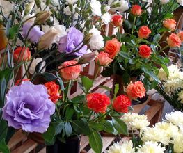 Fiori colorati: rose arancioni e gialle, e fiori viola e bianchi su espositori di legno.