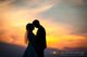 Ein Brautpaar in Silhouette bei Sonnenuntergang, der Himmel in warmen Farben getaucht.