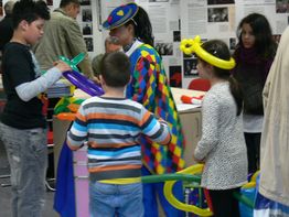 Kinder basteln mit einem clownesken Künstler bunte Luftballontiere auf einer Veranstaltung.