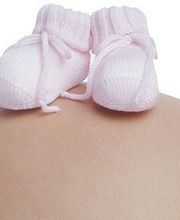 Schwangere Frau mit rosa Babyschuhen auf dem Bauch.