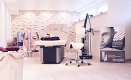 Kosmetikstudio mit Behandlungsstuhl, Geräten und Werbepostern an den Wänden.