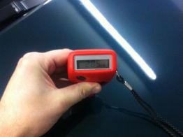 Hand hält ein Lackdickenmesser mit einem roten Gehäuse, Display zeigt "285" auf dunklem Hintergrund.