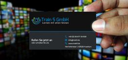 Eine Hand hält eine Visitenkarte von Train 5 GmbH vor einem bunten, unscharfen Hintergrund.