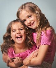 Dos niñas sonriendo y abrazándose, ambas vestidas con camisetas rosas.