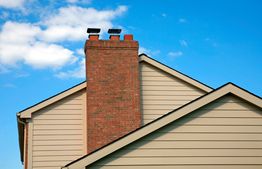 House roof with a brick chimney under a clear blue sky.