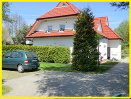 Zweistöckiges Haus mit rotem Dach und geparktem Auto auf einer Auffahrt, umgeben von Bäumen.
