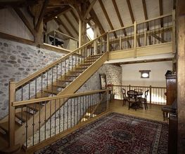 Holztreppe in einem Raum mit Steinwänden, Teppich und einem Tisch im Zwischengeschoss.