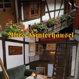 Fachwerkhaus mit Balkon voller Blumen und gemütlicher Innenraum mit Küche und Holztreppe.
