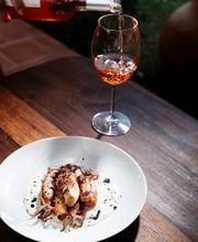 Vinho rosé sendo servido em taça ao lado de prato de frutos do mar em mesa de madeira.