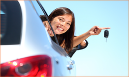 Vrouw glimlacht en houdt autosleutel vast, leunend uit autovenster onder een heldere blauwe lucht.