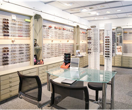Ein Optikergeschäft mit Gläsern und Brillenfassungen auf Regalen und einem Glastisch.