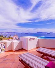 Terraza con vista al mar, piscina y camastros bajo un cielo azul con nubes blancas.
