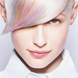 Vrouw met pastelgekleurde haarlok en witte blouse, kijkt naar voren met lichte glimlach.