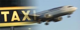 Schild "Taxi" und ein startendes Flugzeug, beide unscharf nebeneinander im Bild.