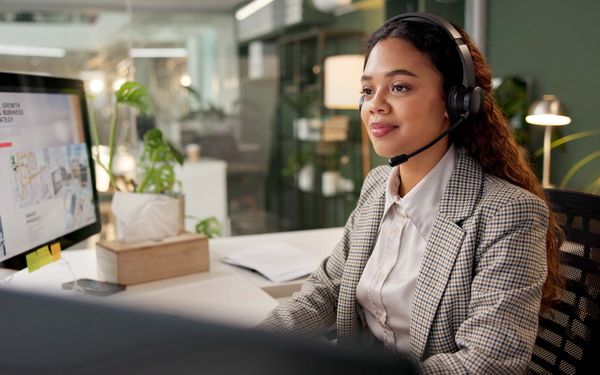 Eine Frau die an ihrem Arbeitsplatz mit Köpfhörern vor ihrem Computer sitzt und als Beraterin im Call Center arbeitet.