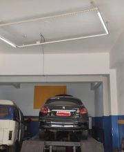 Carro preto elevado em oficina, ao lado de uma kombi branca.