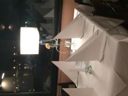 Gedeckter Tisch mit weißem Tischtuch, Kerze, Blume und Lampe in einem Restaurant am Fenster.