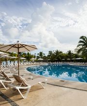 Piscina al aire libre rodeada de palmeras y tumbonas bajo cielos despejados con nubes.