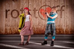 Zwei Kinder posieren vor Holzwand: eins mit rotem Stirnband, das andere macht ein Foto.