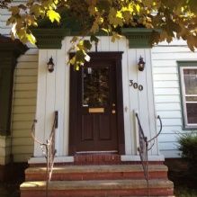 House entrance with a dark door, flanked by lanterns, and number 300 under leafy branches.