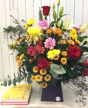 Ramo colorido de flores sobre mesa, con libro amarillo al lado, fondo de madera clara.