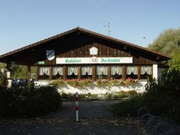 Holzhaus mit Blumenschmuck und Schildern "Bodolzer Dorfstüble" unter blauem Himmel.