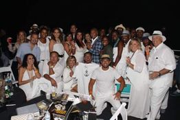 Group of people at a party, dressed in white, smiling and posing together.