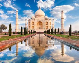 Taj Mahal au lever du soleil avec reflets dans le bassin, ciel bleu et nuages.