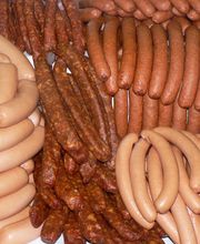 Verschiedene Arten von Würstchen liegen auf einem Tisch, darunter helle und dunkle Sorten.