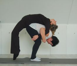 Twee mensen doen een yoga-oefening waarbij de een achterover op de rug van de ander leunt.