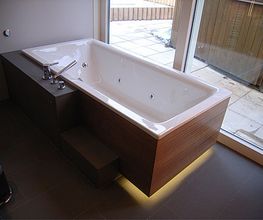 Moderne Badewanne mit Whirlpoolfunktion, Fliesenboden, Holzverkleidung und großem Fenster daneben.