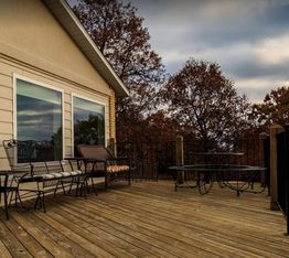 Deck with patio furniture overlooking autumn trees and cloudy sky.