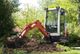 Mini excavator digging in a garden with trees in the background.
