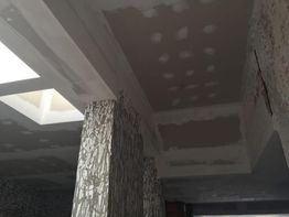 Techo con acabado de yeso sin pintar y columna texturizada en interior de edificio.