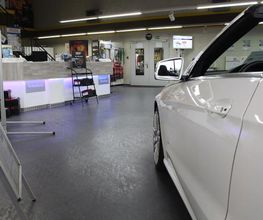 Innenraum eines Autohauses mit weißem Auto im Vordergrund und Empfangsbereich im Hintergrund.