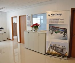 Corredor de escritório com banner da Flottweg e armário branco com planta.