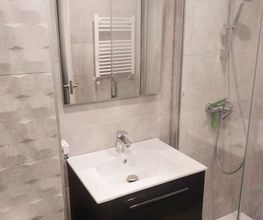 Baño moderno con ducha, lavabo, espejo y paredes decoradas en tonos grises.