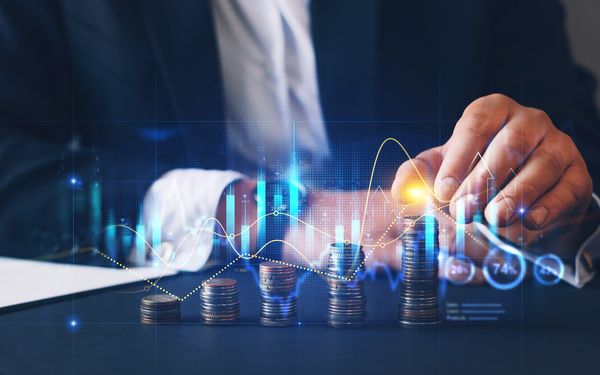 Eine Person in Business-Kleidung stapelt Münzen, während digitale Finanzdiagramme und Kurven das Wachstum und die Entwicklung von Kapital visualisieren.