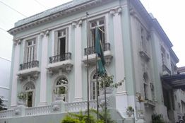 Prédio histórico com fachada branca, janelas altas e bandeira em mastro na frente.