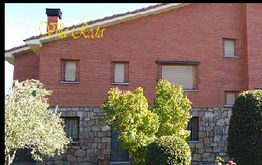 Casa de ladrillo rojo con ventanas pequeñas y jardín de arbustos verdes al frente.